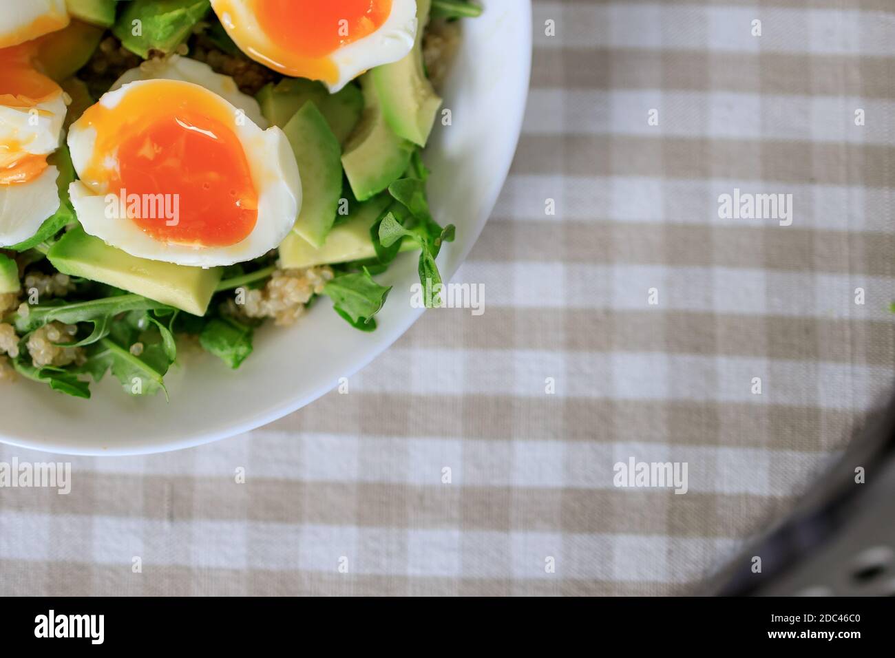 Salad with avocado, quinoa, arugula, soft-boiled eggs on a white plate. Close-up, top view. Healthy, healthy and healthy breakfast concept. Stock Photo