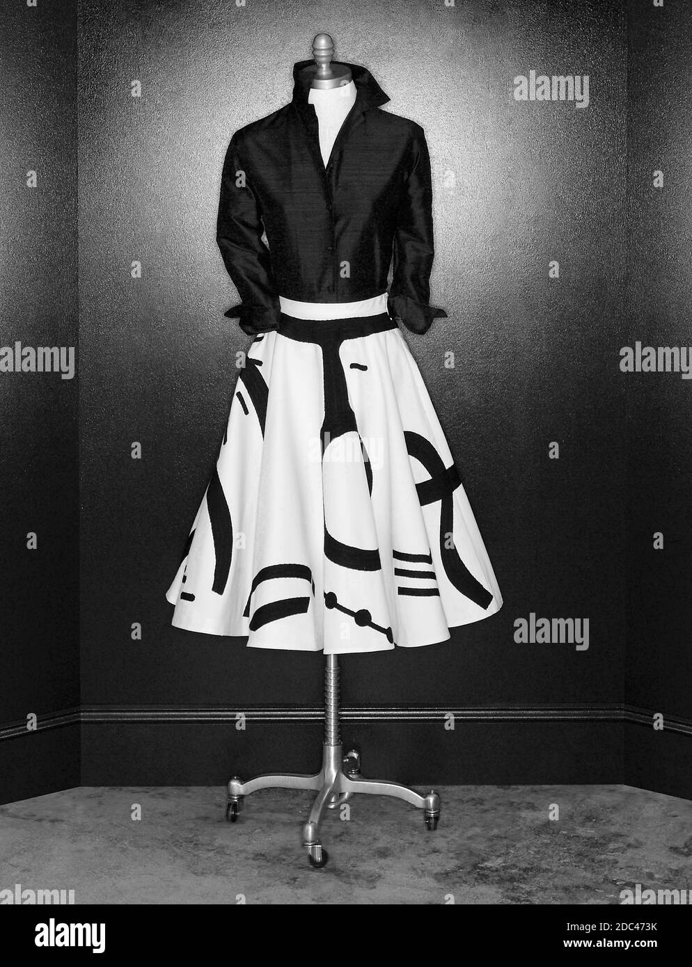 Mannequin with graphic black and white skirt with black top in vertical studio photograph.  Black wall background with glow from ring light. Stock Photo