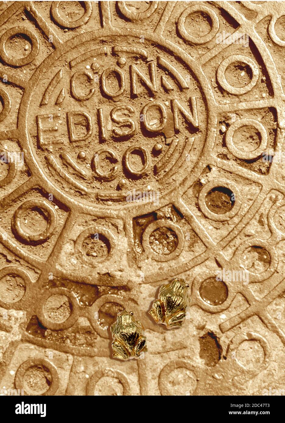 Con Edison man hole cover colored gold with two small golden frogs in this vertical color conceptual photograph. Stock Photo