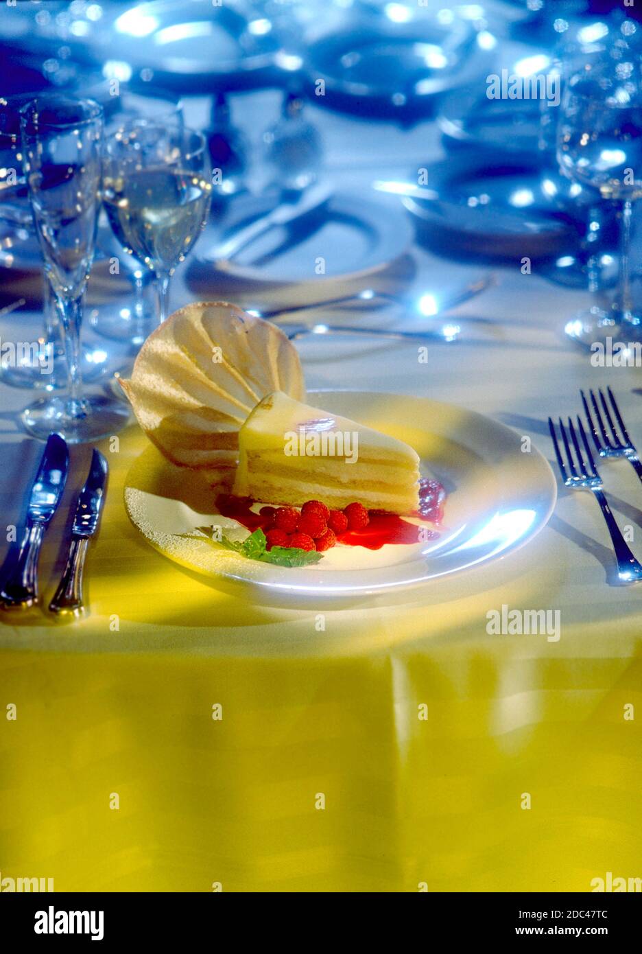 Single slice of gateau layered cake with vanilla cream icing with raspberries in the dramatic vertical photograph.  Formal setting. Stock Photo