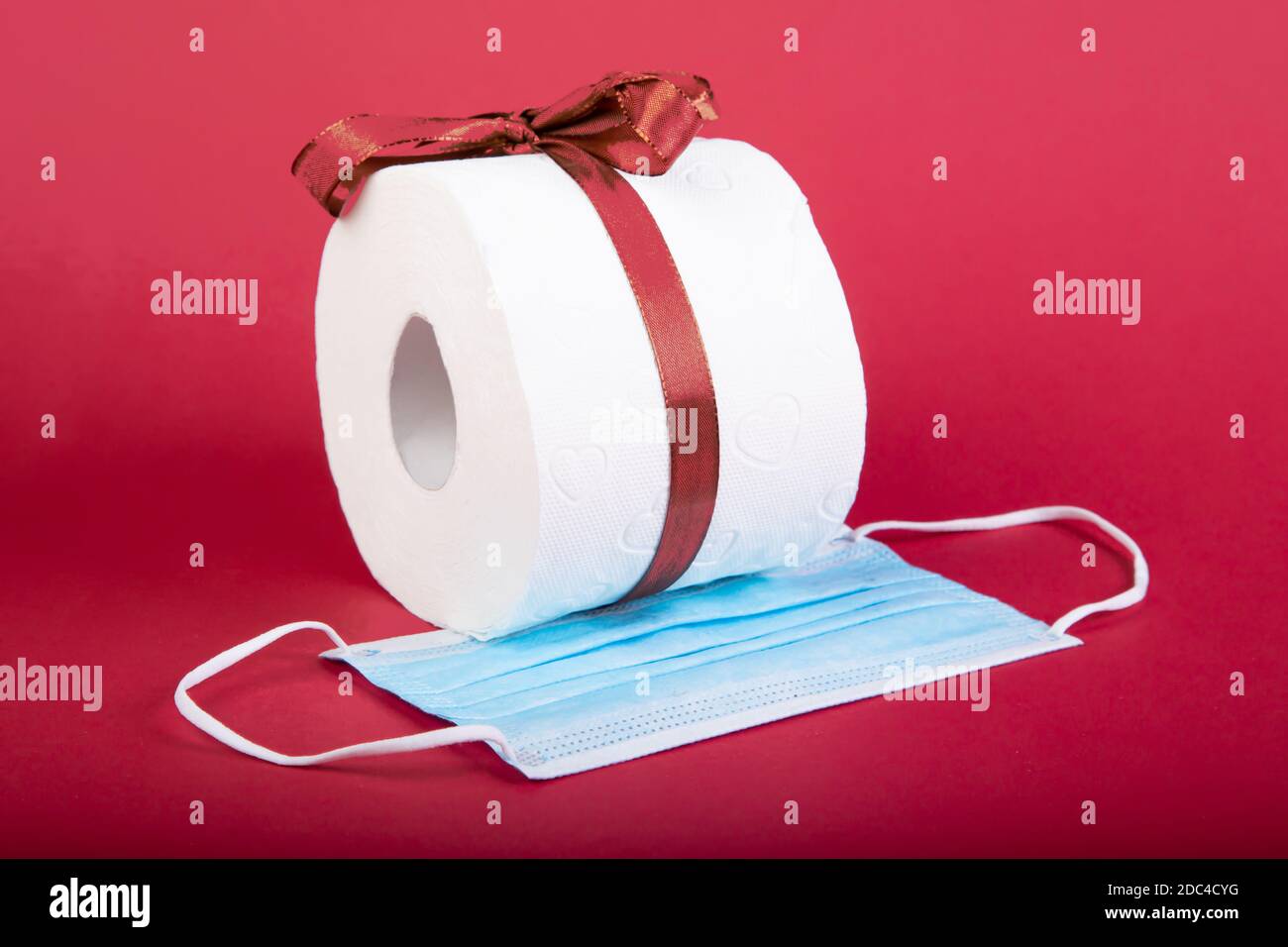 toilet paper roll with loop and a mouth protection mask as christmas present, red background Stock Photo