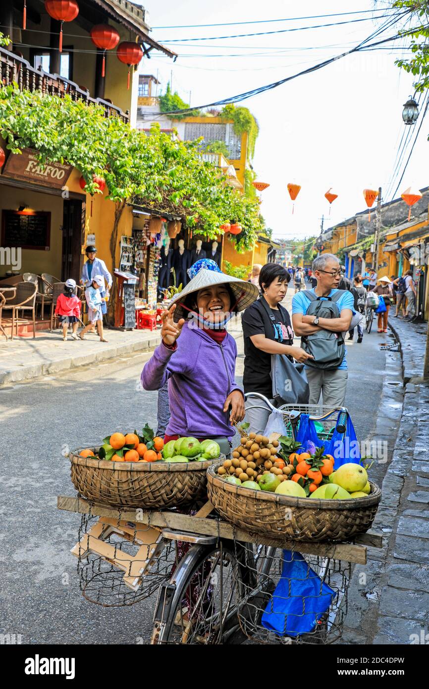 A Vietnamese woman wearing a traditional conical hat, on a bicycle selling fruit on the street, Hoi An, Vietnam, Asia Stock Photo