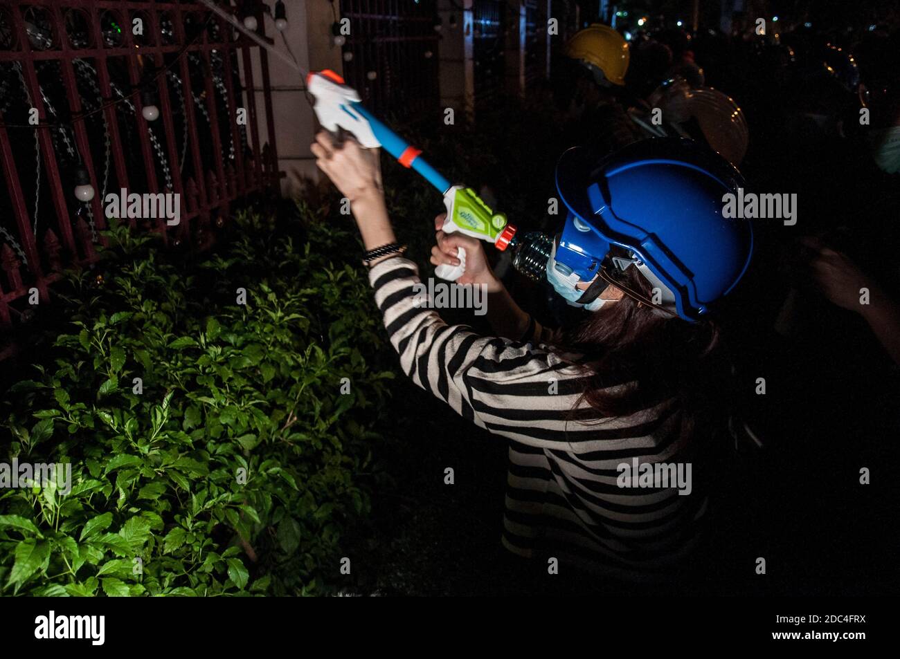 A pro-democracy protester shooting water into the Royal Thai Police Headquarter during the demonstration.Pro-democracy protesters gathered at Ratchaprasong intersection and marched towards the royal Thai police headquarter to splash colour and water following riot police using tear gas and high-pressure water cannons to prevent protesters from approaching Congress during the constitutional debate. Stock Photo