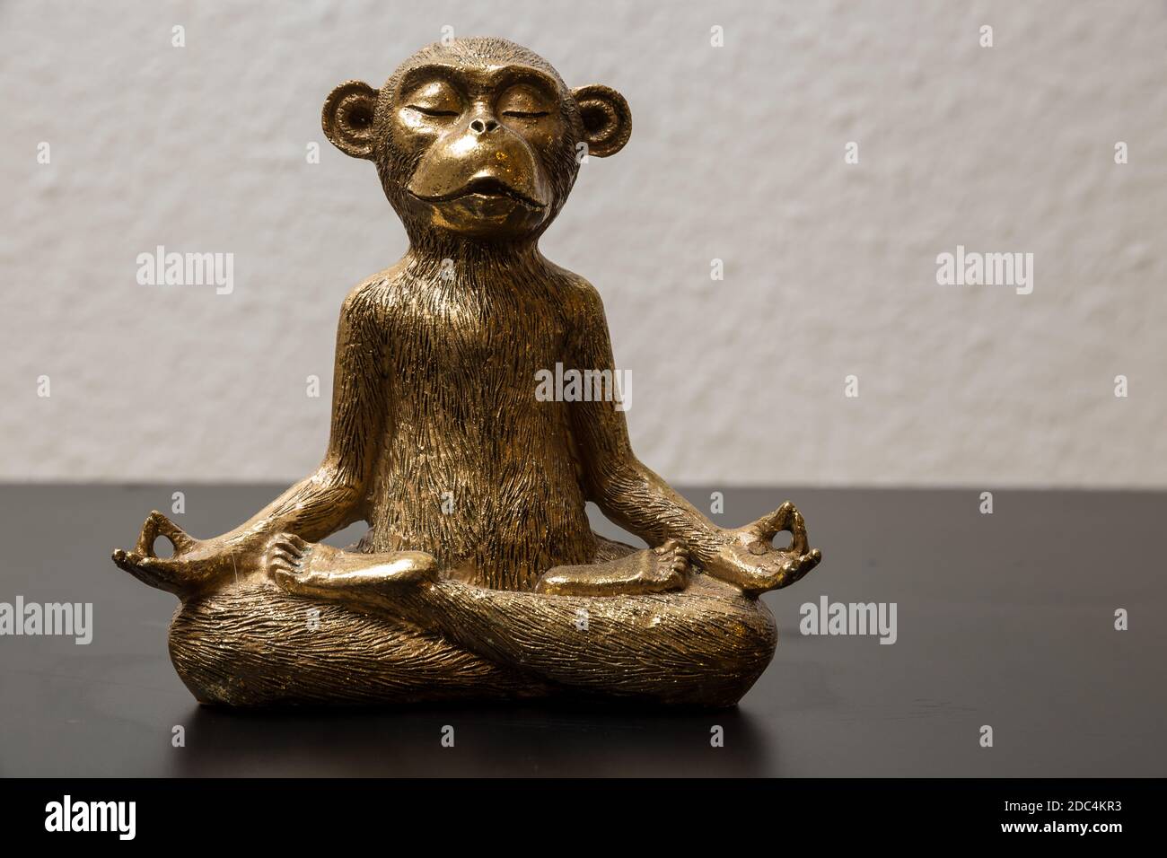 A gold colored meditating monkey statue sitting on a black surface, the
