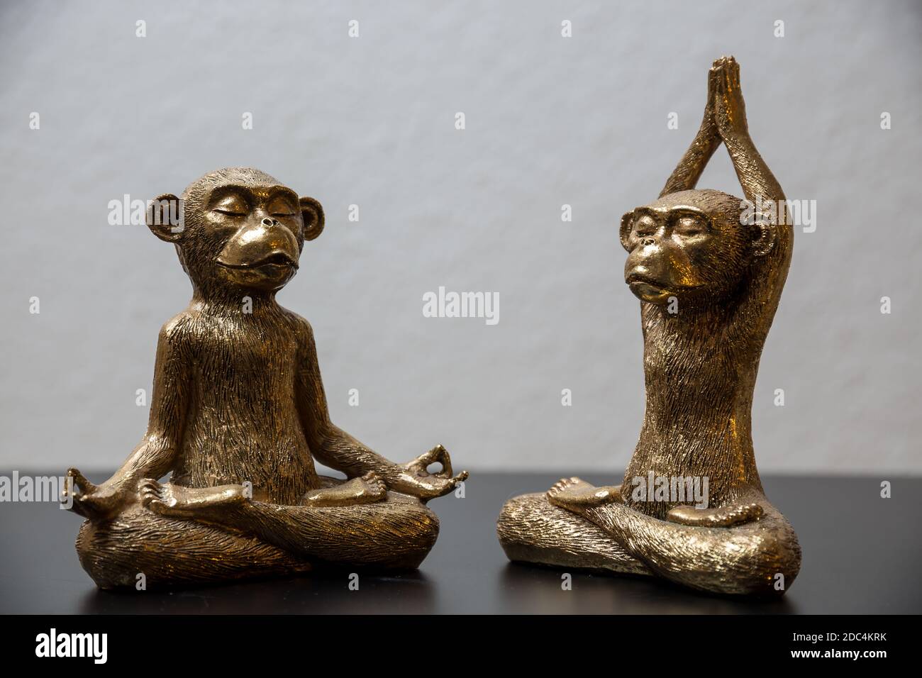 Two gold colored meditating monkey statues sitting on a black surface