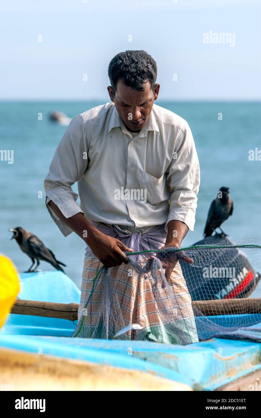 A fisherman gathering a fishing net on Arugam Bay beach in the