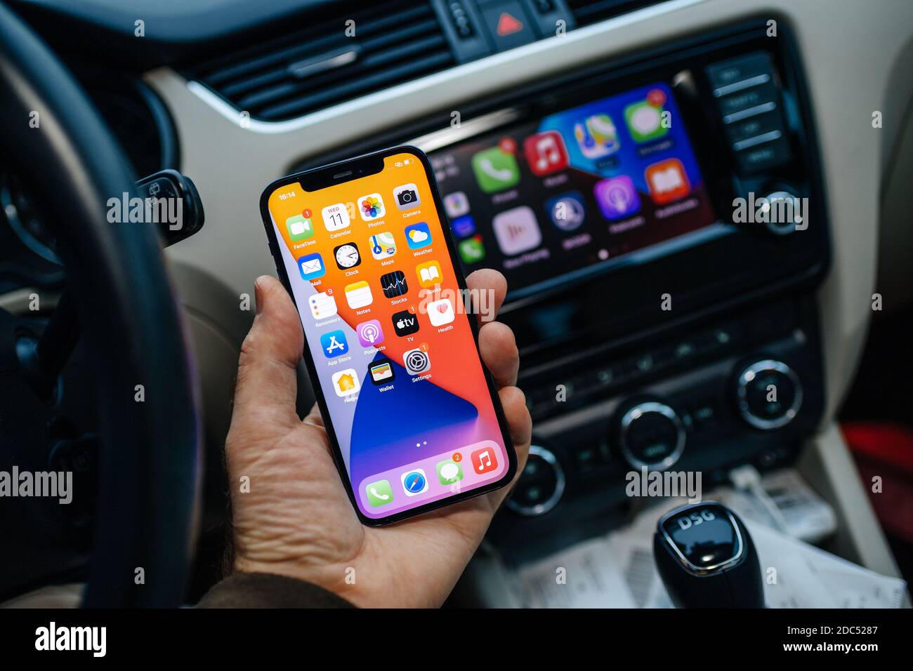 Paris, France - Nov 11, 2020: Male hand holding new iPhone 12 pro with icons of infotainment car computer system running Apple Computers CarPlay from iOS iphone device Stock Photo