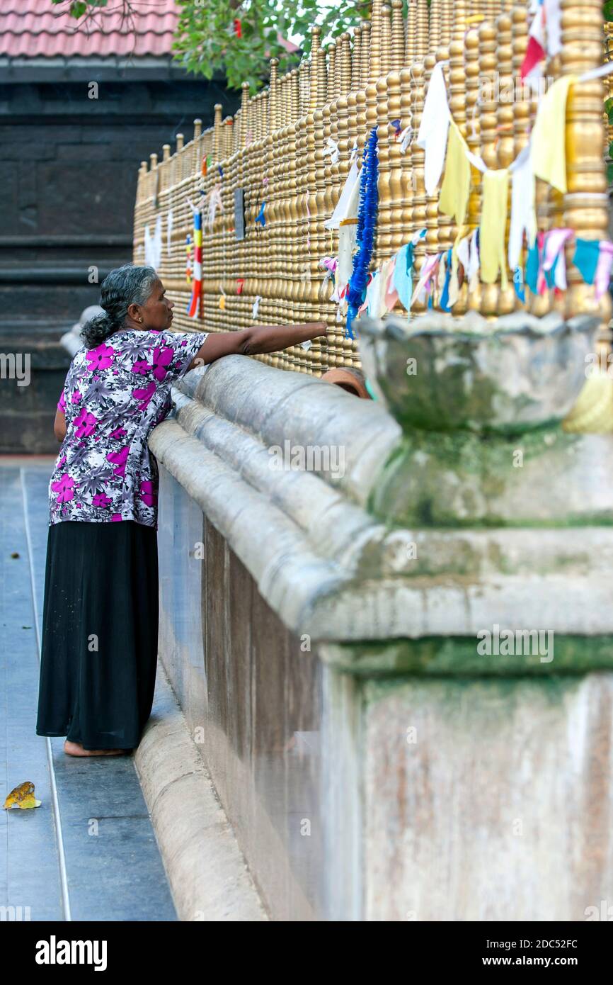 A lady stands next to the sacred Bodhi tree at the Kataragama Temple in southern Sri Lanka. Kataragama is sacred to Buddhists, Hindus and Muslims. Stock Photo