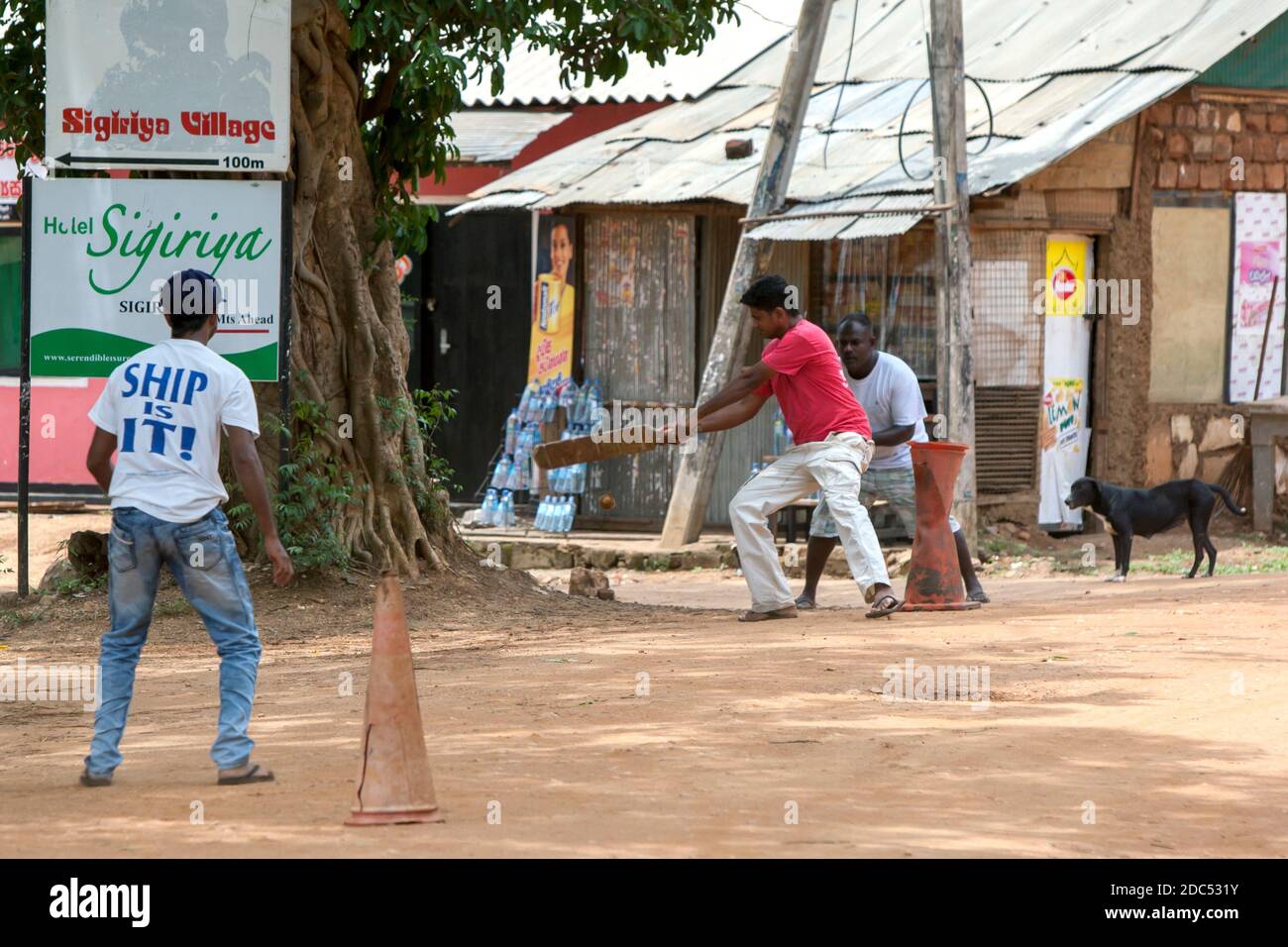 Men playing cricket on a dirt pitch in the street at Sigiriya in Sri Lanka. Cricket is one of the most popular sports in Sri Lanka. Stock Photo