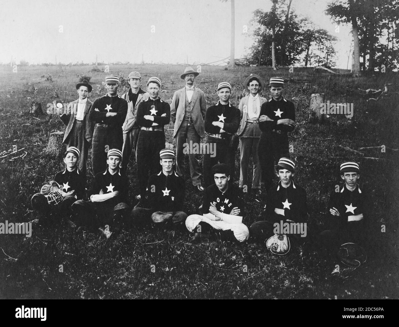 This 1880s baseball team pictures ten players and four coaches or assistants. They are posing in a hillside field, surrounded by tree stumps and grasses. Why they did not pose on their playing field, I don't know. The players wear striped caps, black quilted pants, and pull-over black shirts with a single 5-point star on their chests. But one player's shirt says 'Rome' instead of a star. So, this team may have been from Rome, Wisconsin, USA, since I bought this photograph only a few counties away.     To see my other sports-related vintage images, Search:  Prestor  vintage  sport Stock Photo