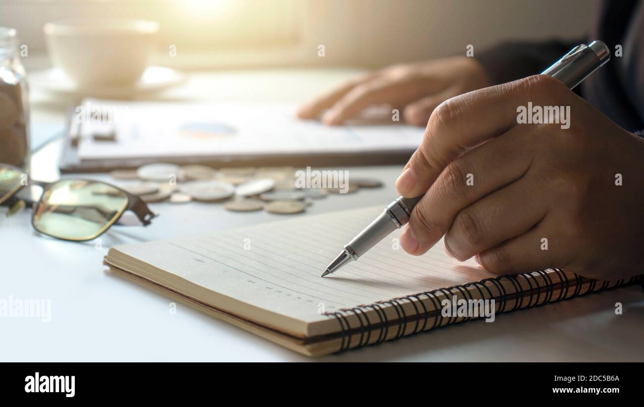 Business people keep notes of income and expenses in a money-saving idea notebook for the future. Stock Photo