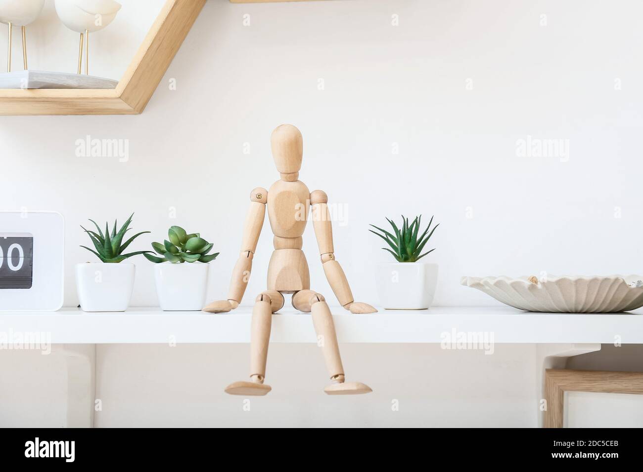 Shelf with wooden mannequin and houseplants on wall in room Stock Photo