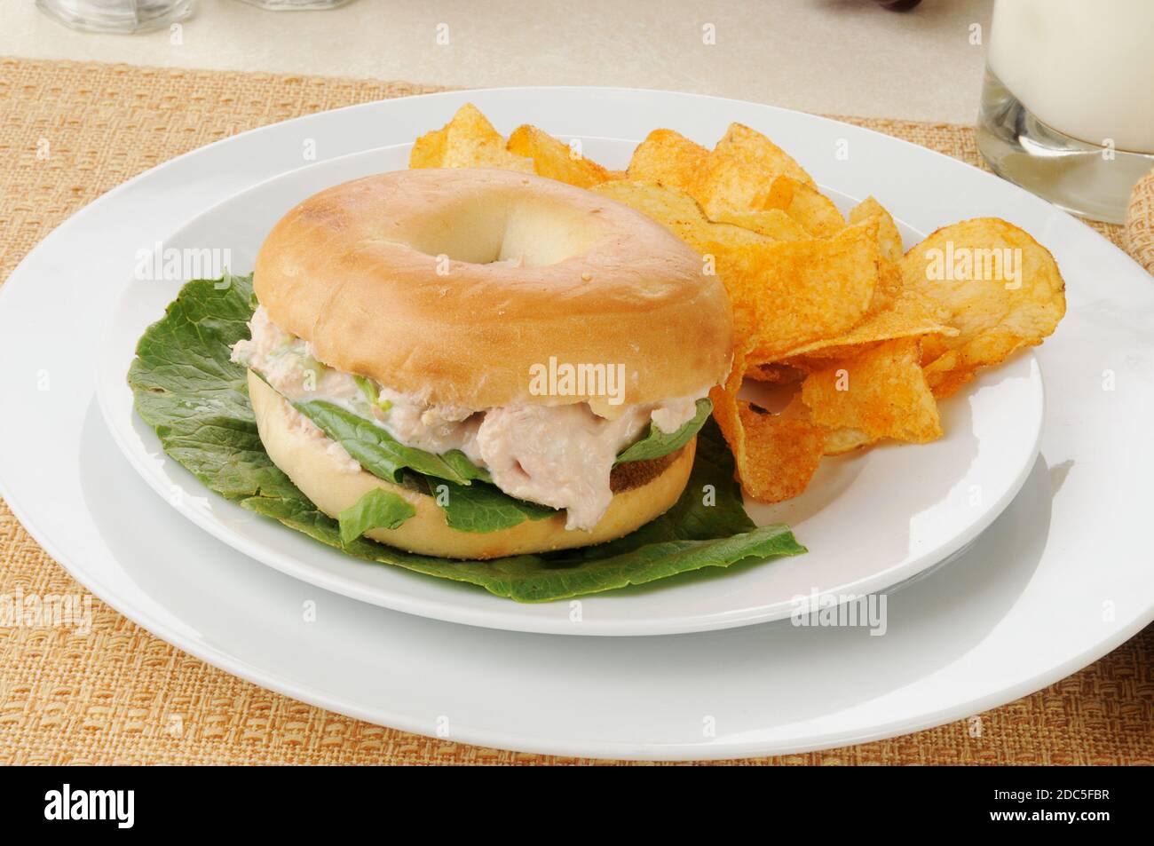 A tuna fish sandwich on a bagel with barbecue flavored potato chips