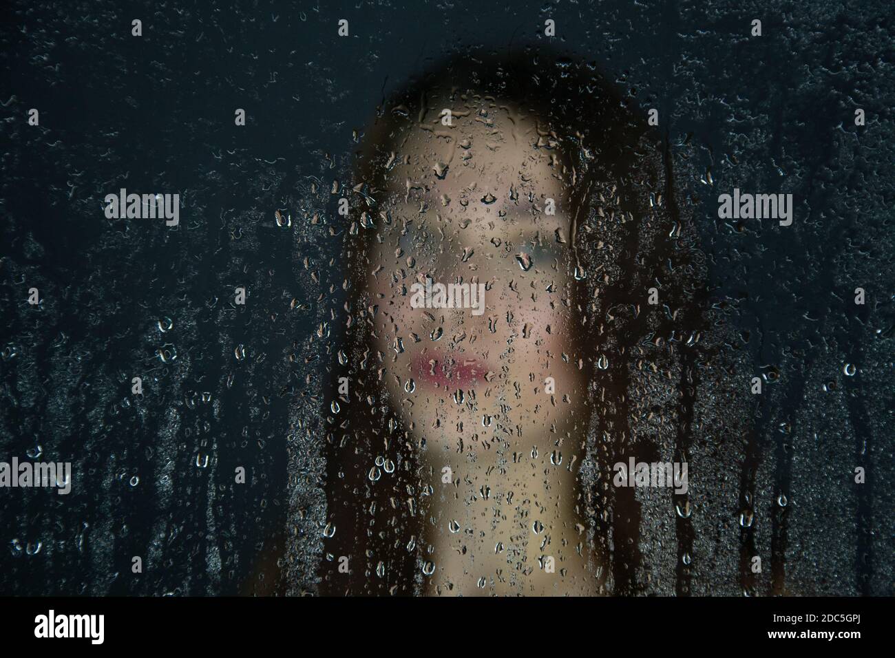 Photo of young girl behind glass with water drops Stock Photo