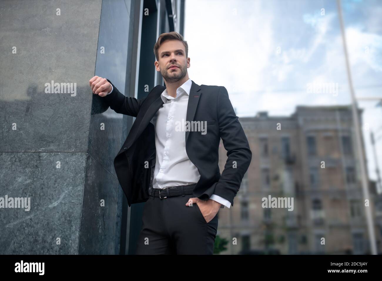 Elegant young man in a black suit posing near the wall Stock Photo - Alamy
