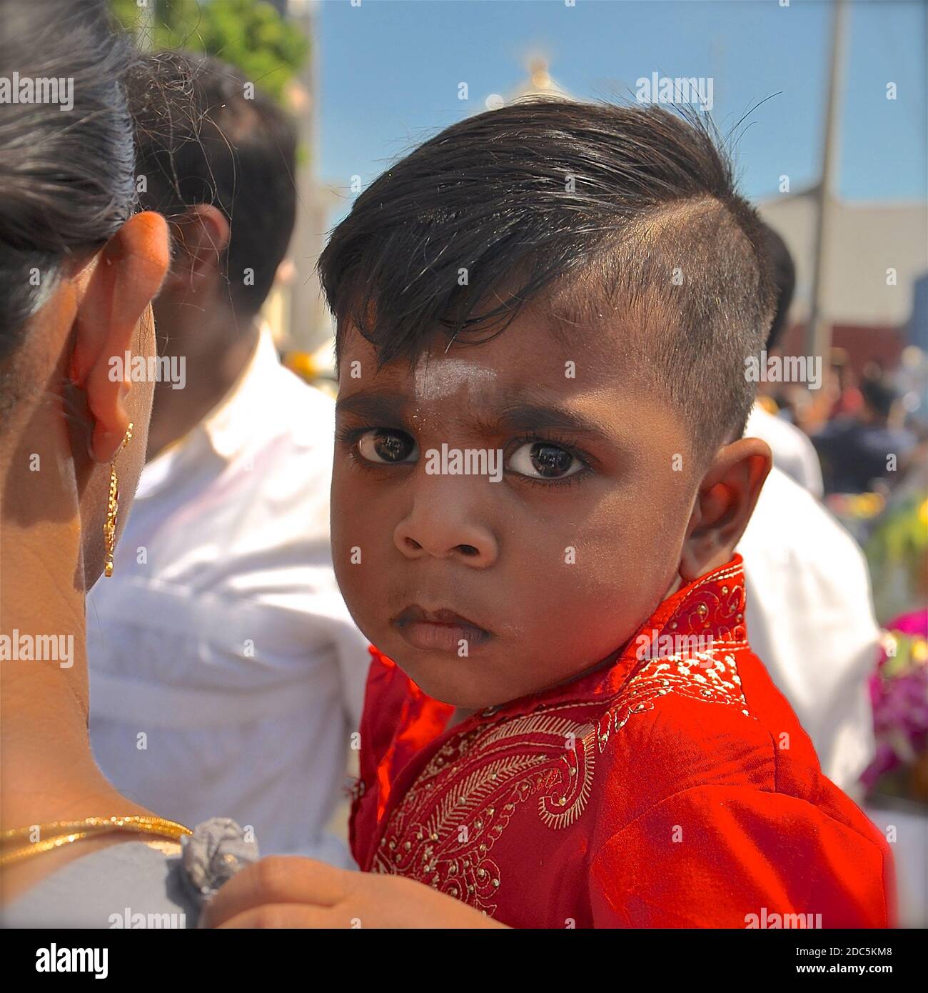 Close up portrait of a young hindu boy with a white bindi, being carried in a parade by his mother. Stock Photo