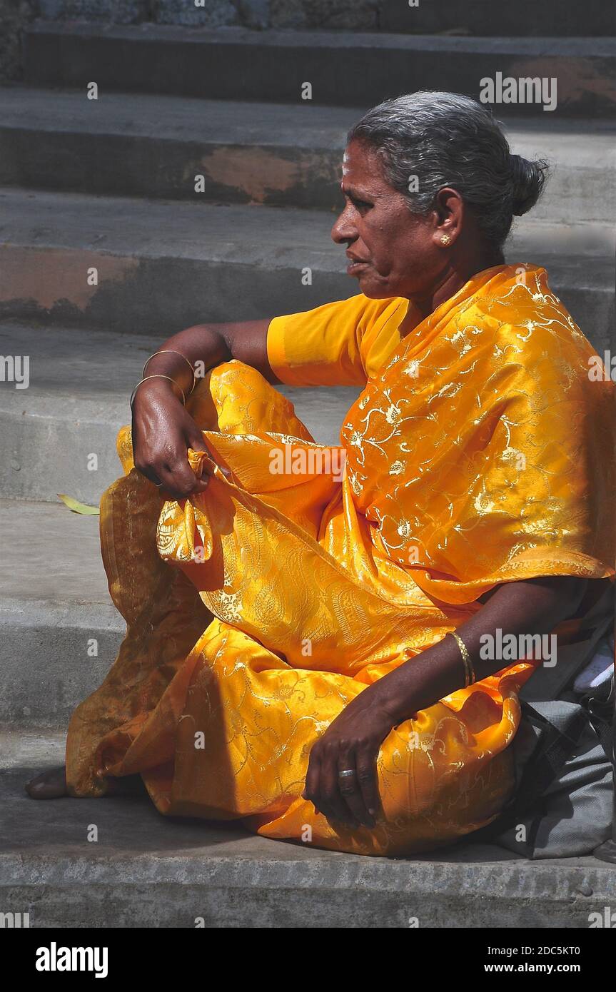 Indian lady in a golden sari sitting waiting on some stone steps. Stock Photo