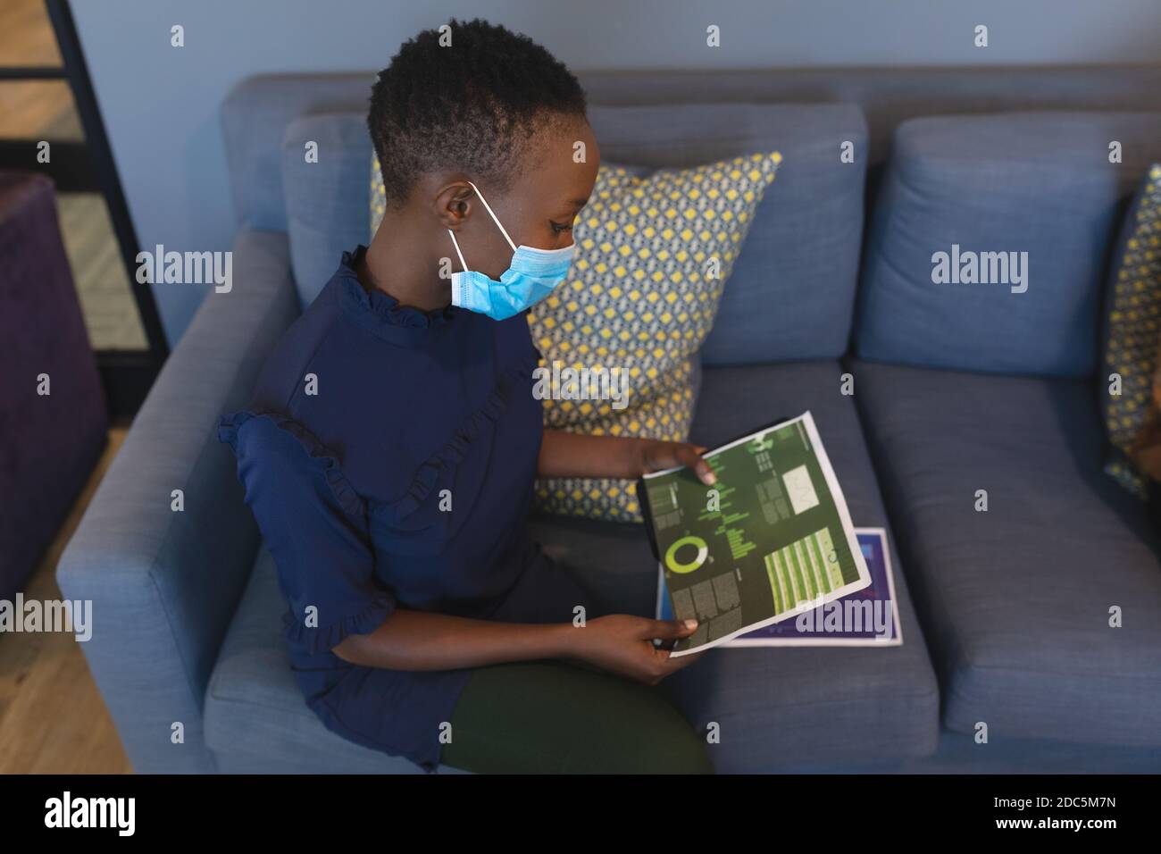 African american woman wearing face mask reading documents at modern office Stock Photo