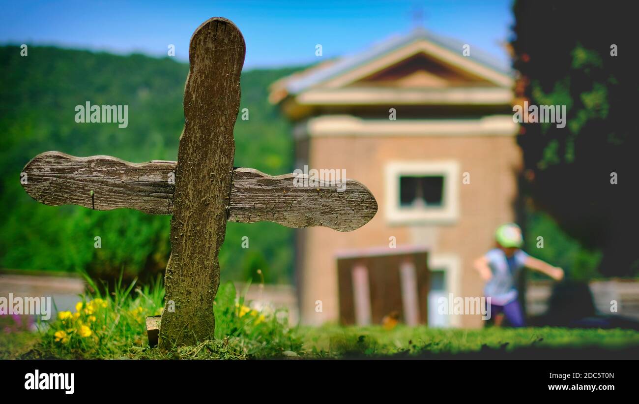 old wooden cross in cemetery with small church on sunny day with little girl running in background Stock Photo