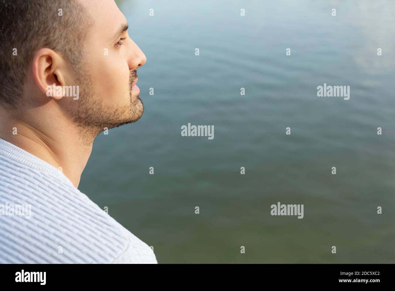 Thoughtful, serene young man at lakeside Stock Photo
