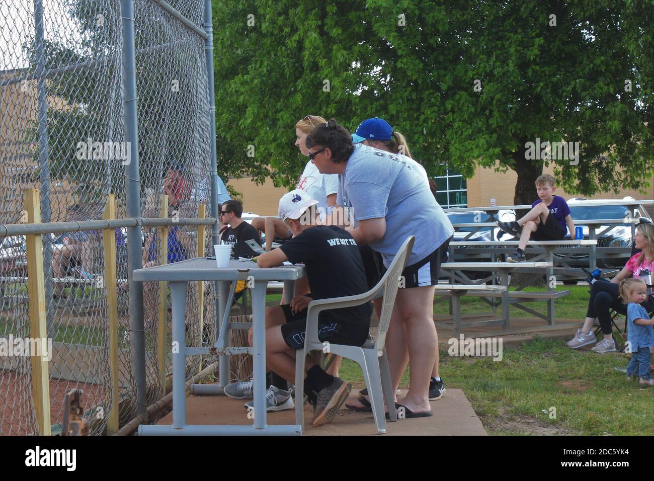 Girls Softball Game score keepers behind the chain link fence on a summer day in Kansas. Stock Photo