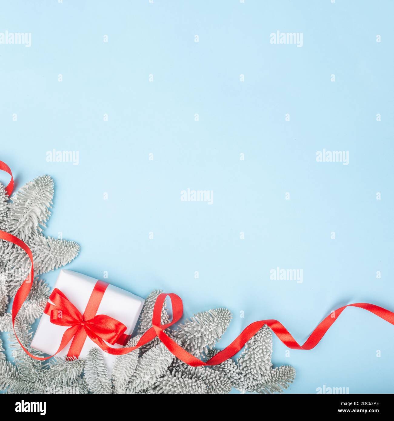 Frosted fir tree twigs and Christmas decorative gift with red ribbon on blue background with copy space for text template flat lay top view design Stock Photo