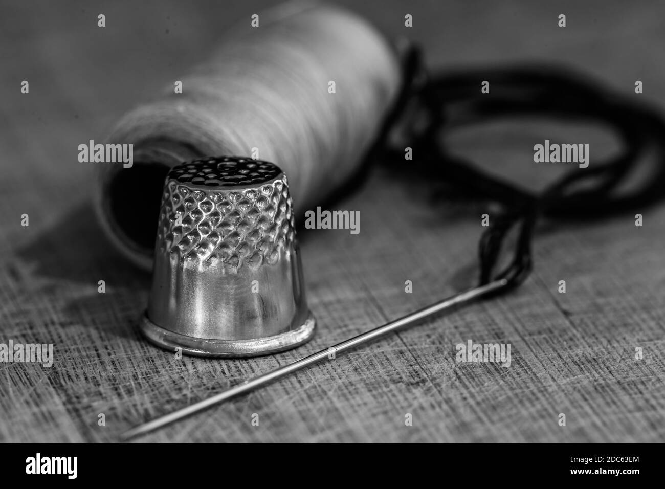 A grayscale shot of thimble and needle on wooden background Stock Photo
