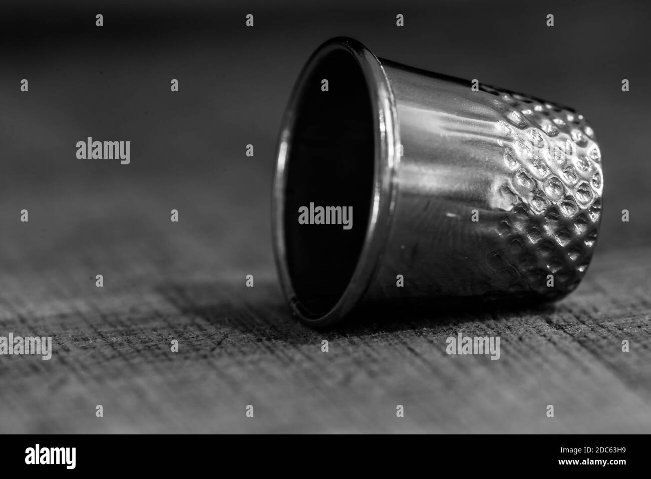 A grayscale shot of thimble and needle on wooden background Stock Photo
