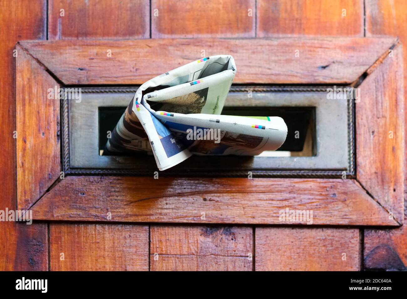 newspaper, paper, tabloid folded up and stuffed into a mail slot of a wooden door at street level concept journalism, communication, news, post, mail Stock Photo