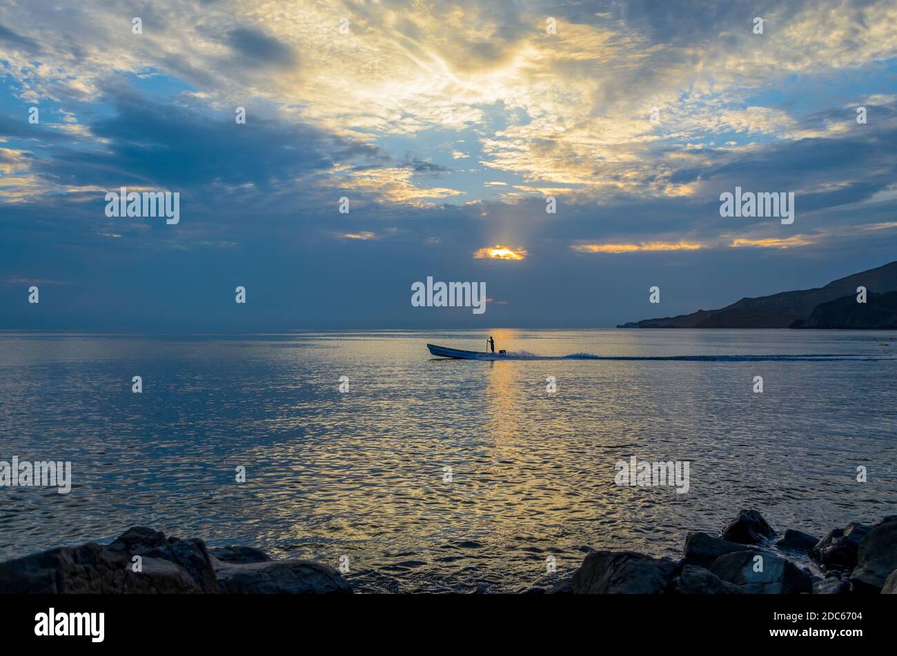 Silhouette of a lone fisherman in a fishing boat starting for work during the first light in the morning. Stock Photo
