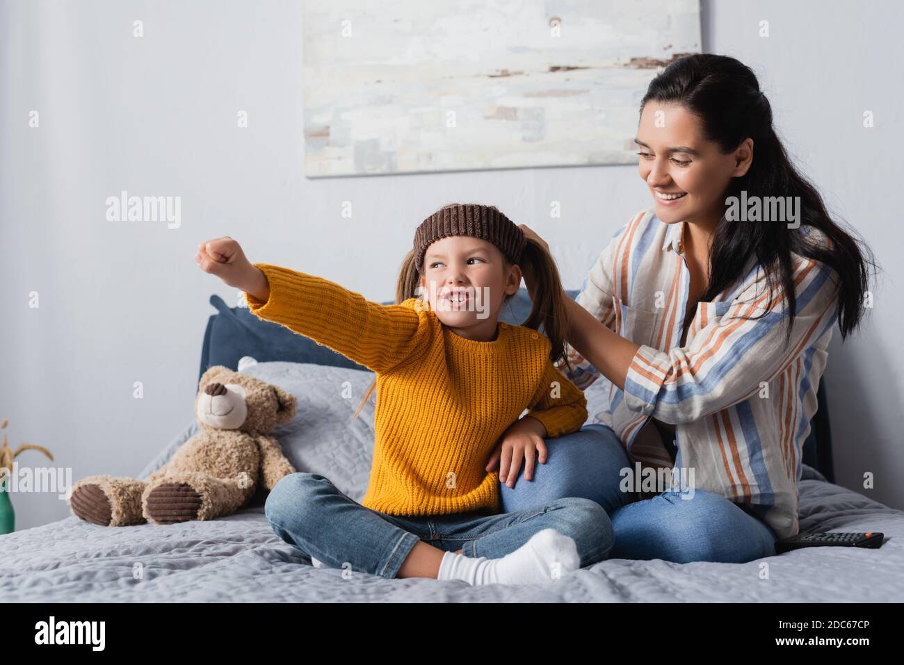 excited girl in headband grimacing with outstretched hand near smiling mother Stock Photo