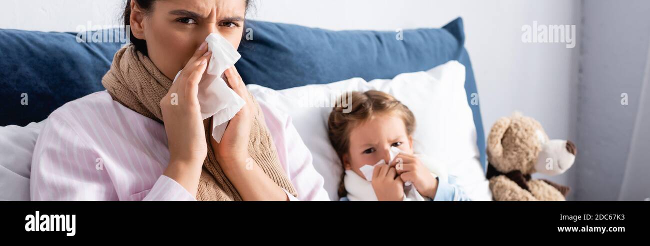 ill child and mother with runny nose sneezing in paper napkins, banner Stock Photo