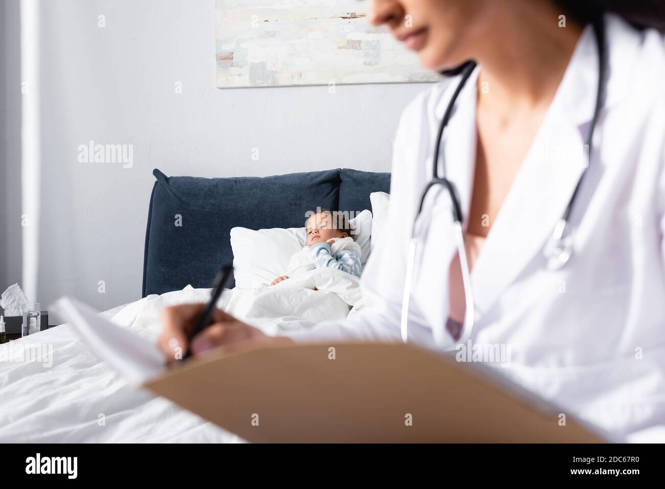 ill child lying in bed while pediatrician writing diagnosis on blurred foreground Stock Photo