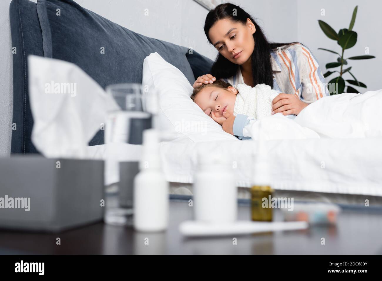 mother hugging sick daughter sleeping in bed near bedside table with medicines on blurred foreground Stock Photo