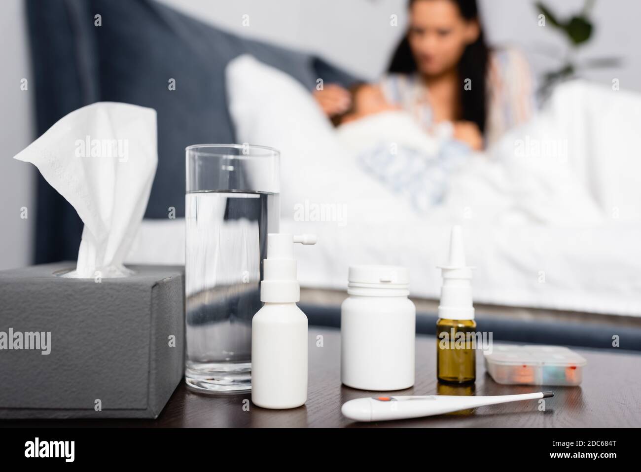 bedside table with medicines, glass of water and thermometer near sick child lying in bed near mother Stock Photo