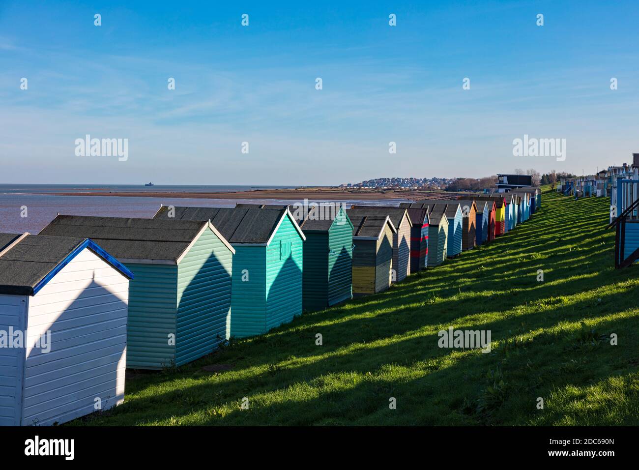 Rows of colourful beachuts cast strong shadows of hut shapes on the huts in front on the shore of the Thames Estuary, Tankerton, Whitstable, Kent, UK Stock Photo