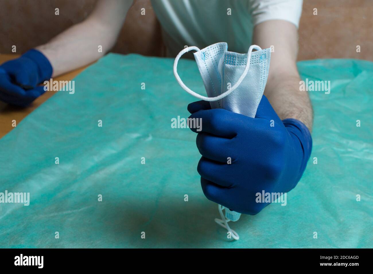 A closed fist protected with blue gloves squeezes a surgical mask. Health care and surgical concept. Personal protective equipment in healthcare. Stock Photo