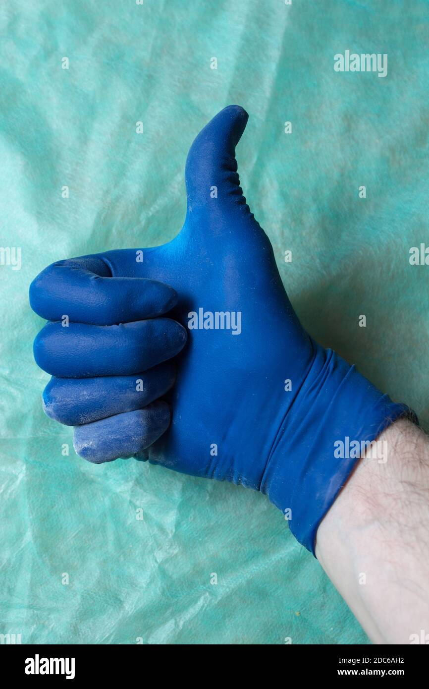 A blue glove hand with the thumb up as a sign of approval with a green surgical fabric background. Health care and surgical concept. Stock Photo