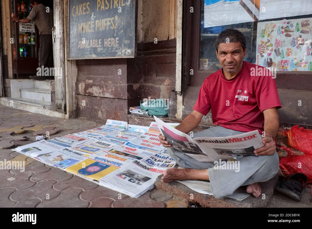 A newspaper vendor in Byculla, Mumbai, India, with his small selection of newspapers in English, Hindi and Marathi spread out on the sidewalk Stock Photo
