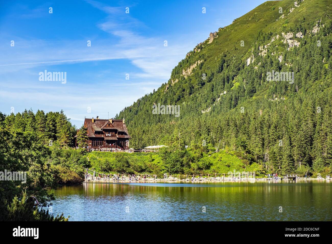 Panoramic view of the Morskie Oko mountain lake surrounding larch, pine and spruce forest with Schronisko przy Morskim Oku shelter house in background Stock Photo