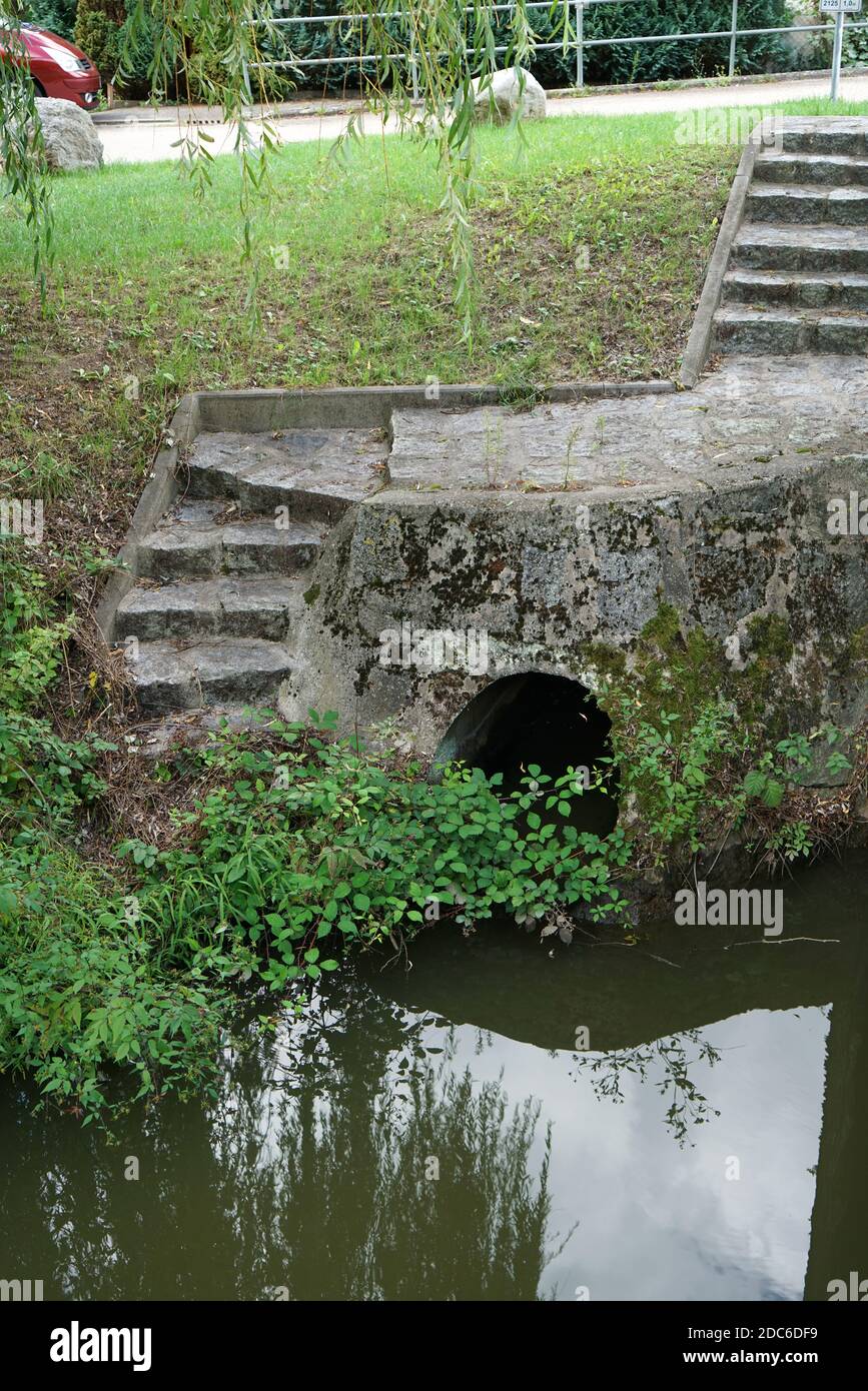 A view of a tiny water tunnel with stairs above in the field with plants and trees Stock Photo