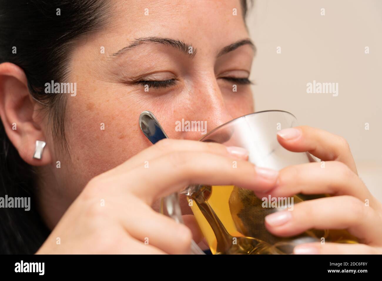 Close-up of ill female model drinking hot medical tea from glass mug as covid19 virus infection cold or flu treatment pandemic concept Stock Photo