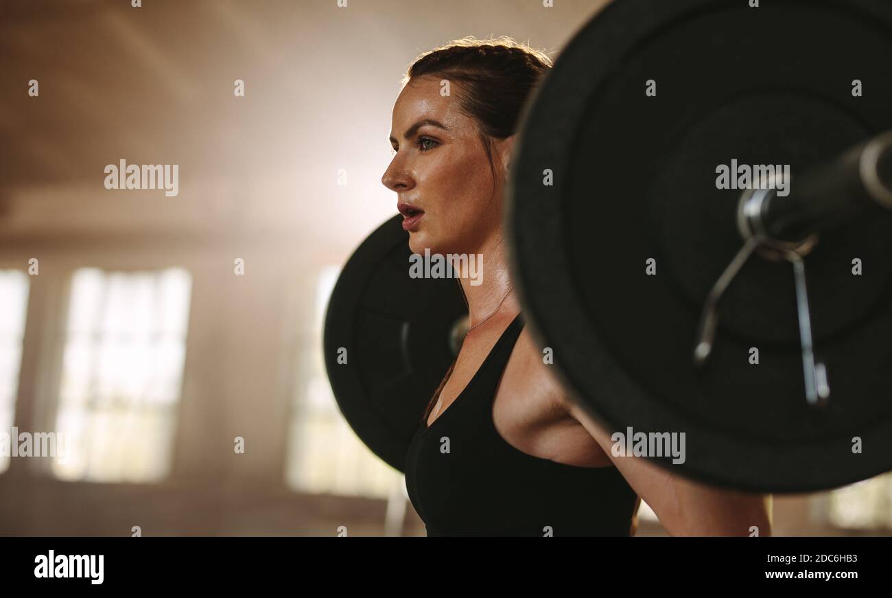 Back view of strong female athlete reflecting in mirror in gym and