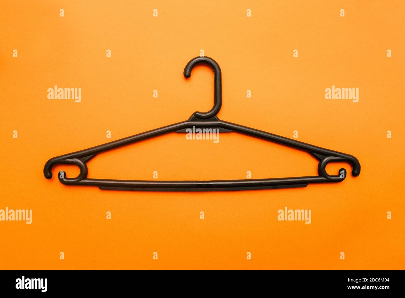 Black clothes hanger isolated on orange background. Empty plastic hanger for shop and home. Holder for shirts, coats, dresses and other items. Shoppin Stock Photo