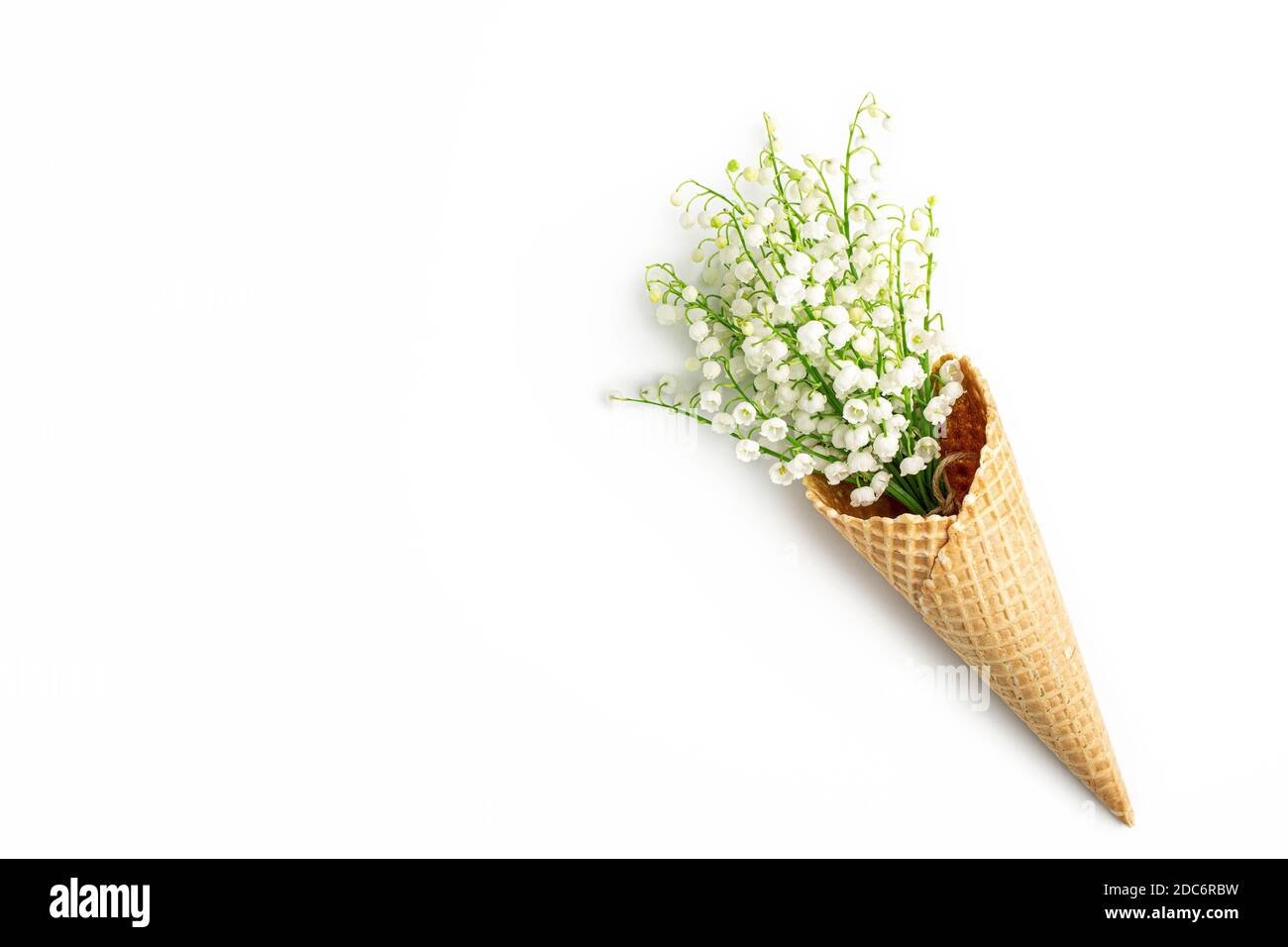 Bouquet of lilies of the valley in a waffle cone on a white background. Ice cream cone with spring flowers. Greeting card. Copy space, flat lay, top v Stock Photo