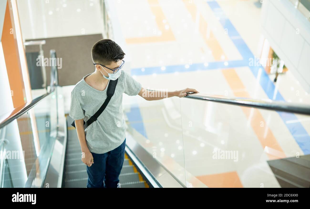 Teenage boy 12 years old wearing face mask on escalator in shopping mall Stock Photo