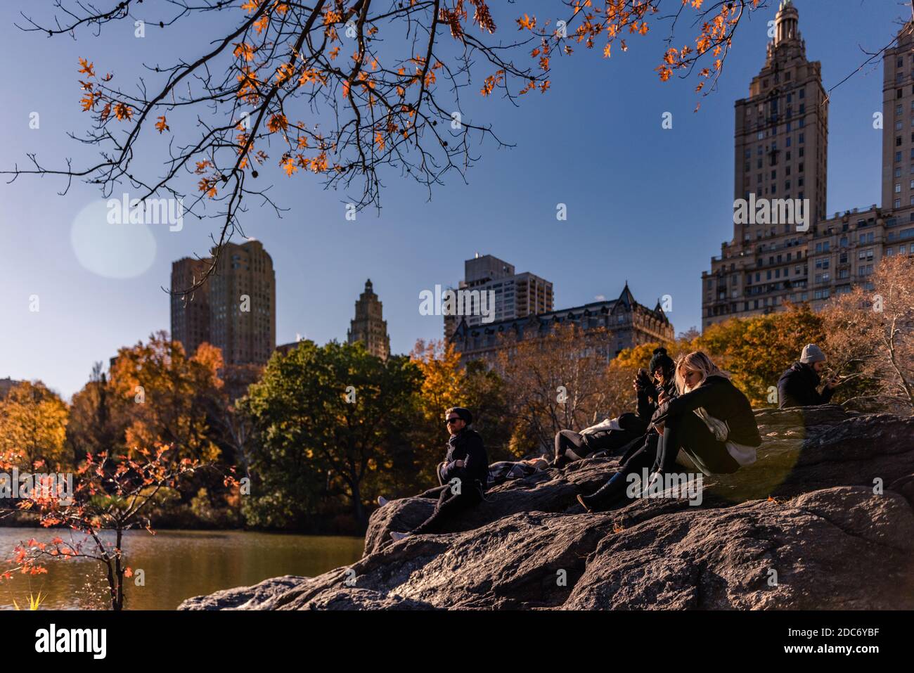 People relaxing on the rocks while they are looking at lake in Central Park in sunny day Stock Photo