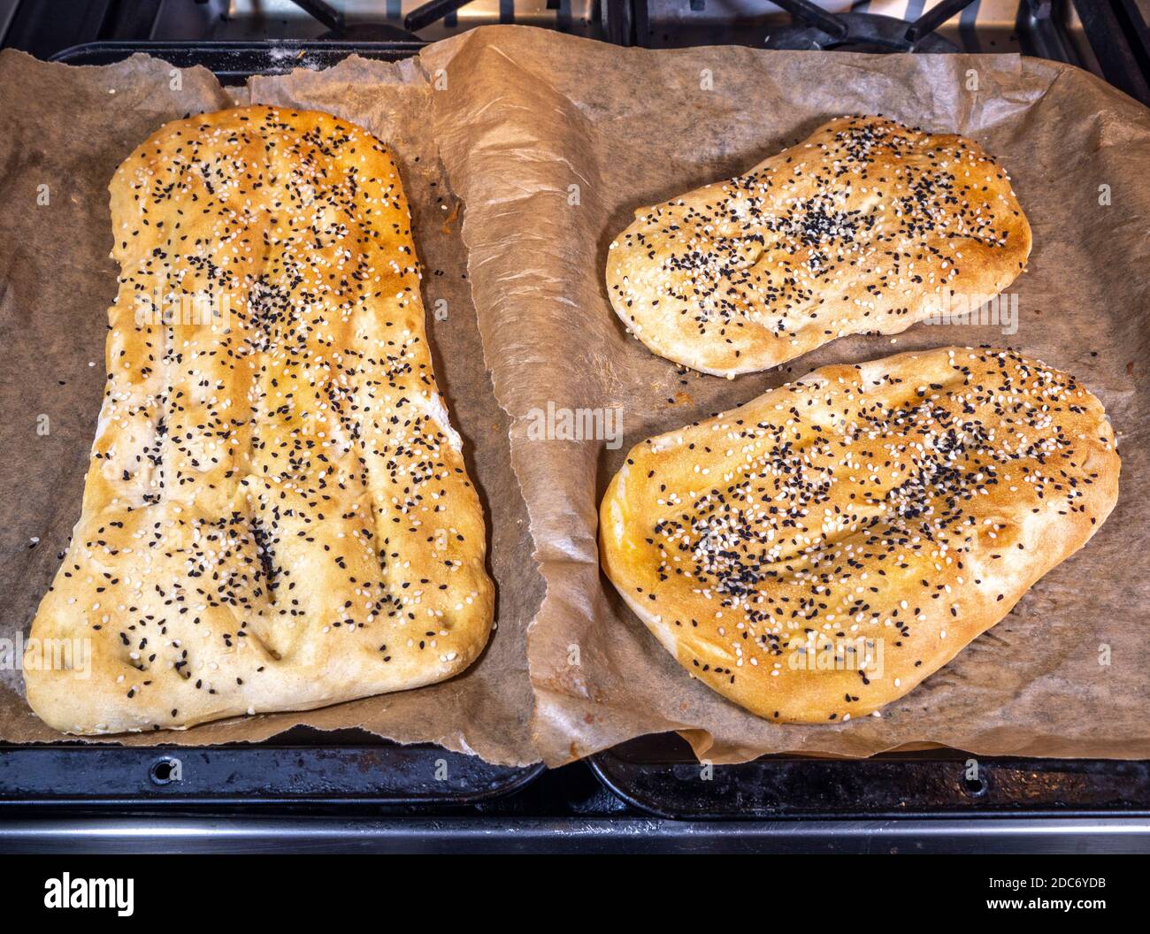 Hot pieces of Persian barbari flatbread (yeast leavened Iranian flatbread), topped with nigella and sesame seeds, on sheets of baking parchment. Stock Photo