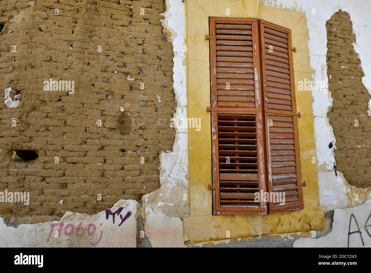 Old handmade clay and straw mud bricks exposed in house wall with shuttered dressed stone surround of window Stock Photo