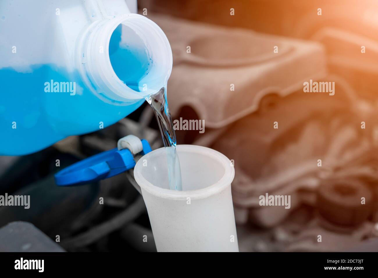 Pouring liquid from plastic canister into car washer fluid reservoir